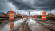© john - Construction zone with orange traffic cones and idle excavation equipment under overcast sky showing recent rain and muddy ground