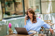 © sepy - Brunette haired woman sitting in an outdoor cafe and using smarpthone and computer laptop