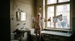 © Oleksandr - Blonde Woman in Lingerie Hanging Laundry in a Distressed Bathroom with a View to the Street, Creating a Surreal and Evocative Image