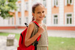 © sementsova321 - A joyful young girl with a red backpack smiles at the camera, looking forward to the first day of school.