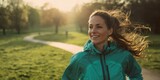 The woman jogging happily in a sunlit park on a beautiful day.
