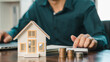 © ภาคภูมิ ปัจจังคะตา - Real estate investment and mortgage calculation concept with businessman using calculator, coins stacked on desk, laptop, and small house model, representing property finance, budget planning, and hom