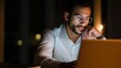 © Johannes - focused young indian ethnic business man student or web designer working on laptop computer late at night at home or in dark office thinking watching webinar learning online course sitting at desk no