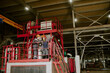 © AnnaStills - Two middle aged Caucasian women wearing safety helmets standing on industrial platform discussing machinery operation inside large factory building with metal structures visible