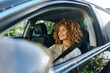© SHOTPRIME STUDIO - Smiling woman driving car fastened with seatbelt, curly hair, casual clothing, daylight, safe urban travel, joyful expression, natural light.