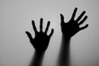 © Begum - Silhouette of Two Hands Reaching Out from Behind a Frosted Glass Surface in a Dark and Mysterious Setting