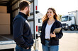© Alex & M Studio - Female manager with a tablet discusses logistics with a delivery driver standing at the open back of a truck full of cardboard boxes for a moving or shipping service