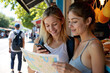 © Alex & M Studio - Two happy young female friends navigate a foreign city together on vacation, one using a traditional paper map and the other a smartphone for directions and guidance