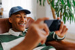 © BONNINSTUDIO/Stocksy - Happy man playing video games on smartphone at home