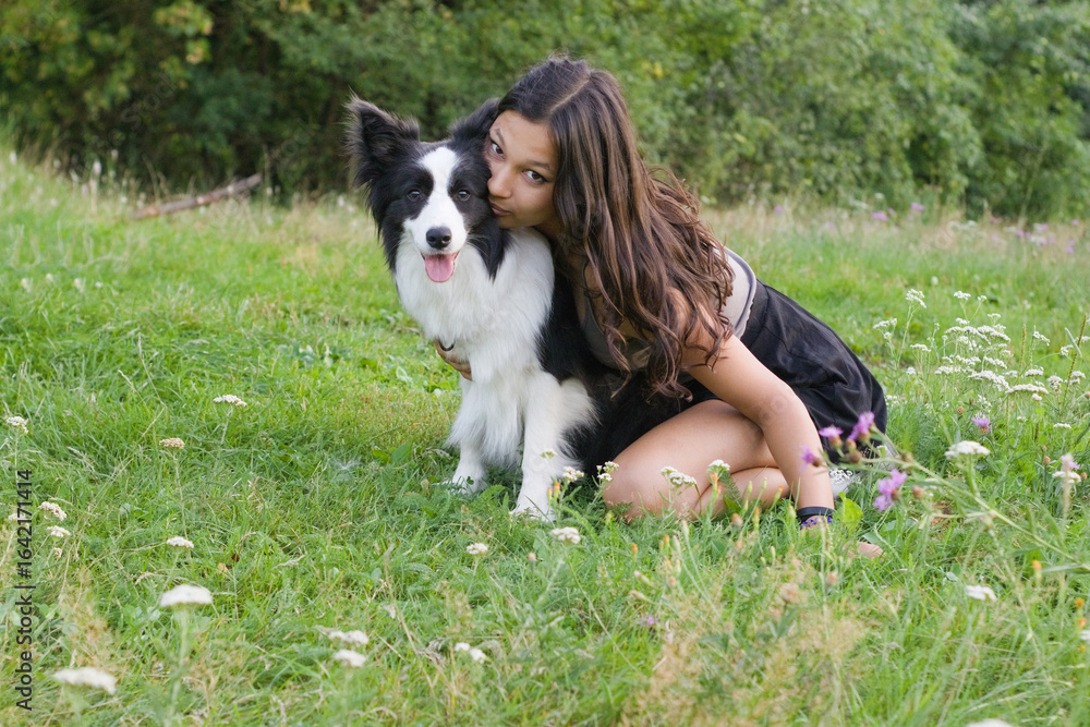 Young woman embracing Border Collie dog in meadow, leaning in with affection. Ideal for pet love themes, canine companionship visuals, and natural lifestyle portrait photography