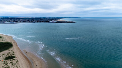 Wall Mural - Aerial view of coastal town with sandy beach and calm ocean on overcast day.