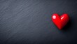 © Husen - A single, glossy red heart rests on a dark slate background.