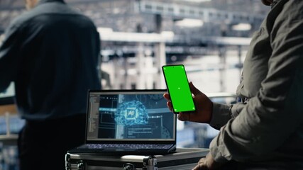 Technician using green screen smartphone in server hub while optimizing deep learning systems handling tasks. Data center worker uses chroma key phone, adjusting AI model parameters