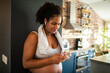 © Davor - Pregnant woman relaxing after home workout using phone and earbuds in kitchen