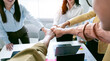 © NAMPIX - A diverse team of business professionals celebrates a successful project by stacking their hands together in a gesture of unity and teamwork.