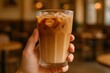 © Thanakrit - Iced coffee with milk, cold beverage with ice cubes, hand holding a glass of iced coffee