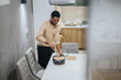 © qunica.com - A man prepares food in a kitchen, stirring the contents of a pot on a dining table in a contemporary domestic interior.