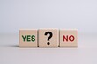 © The Little Hut - Decision Making Concept: Wooden Blocks Displaying Yes, No, and Question Mark on Neutral Background