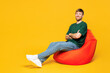 © ViDi Studio - Full body young smiling happy man wear green t-shirt casual clothes sit in bag chair hold hands crossed folded look camera isolated on plain yellow orange background studio portrait Lifestyle concept