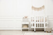 © New Africa - Comfortable crib, pouf, bedside table and toys near white wall in baby's room. Interior design