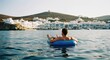© SugarStock - Man on float relaxing in sea with Greek village view