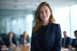 © Enrique - Successful businesswoman wearing a blue suit jacket, in her office, with her management team in the background and out of focus.