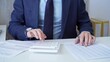 © volha_r - Businessman accountant with blue suit is using white calculator and taking notes with a silver pen. Taxes and audit concept