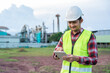 © tong2530 - Asian engineer in safety helmet and reflective vest using a tablet at an industrial site, representing construction management, inspection, and modern engineering technology.