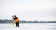 © Dmitry - Male surveyor working with total station measuring equipment on tripod in snowy field during winter. Geodesy concept for construction project.