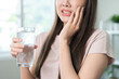 © KMPZZZ - Suffering from toothache, hurt asian young woman touch cheek, face expression ache or feel pain, sensitive molar teeth, hand holding glass of water with ice, inflammation when drink cold, healthcare.