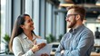 © jow - Two colleagues sharing ideas in a modern workspace with a friendly interaction and soft background.