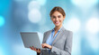 © wipawan - Young female executive in elegant gray business suit with laptop computer, cheerful expression, professional hairstyle, blue blouse, clean minimal background with blue and white tones