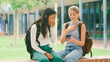 © Monkey Business - Two Female High School Or Secondary Students Looking At Social Media On Phone Sitting Outdoors