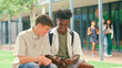 © Monkey Business - Two Male High School Or Secondary Students Looking At Social Media On Phone Sitting Outdoors