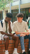 © Monkey Business - Two Male High School Or Secondary Students Looking At Social Media On Phone Sitting Outdoors
