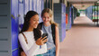 © Monkey Business - Two Female High School Or Secondary Students Looking At Social Media Or Internet On Phone By Lockers