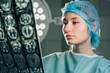 © Vladislav - Female surgeon in operating room, wearing surgical cap and gown, examining brain scan images under bright surgical lights, showcasing dedication to patient care and medical expertise