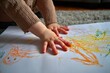 © YanabY - Child engages in creative drawing with crayons on paper while seated on a cozy rug indoors during daylight