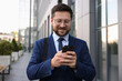© New Africa - Successful businessman with smartphone near office building