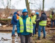 © Lefanya - Resilient woman leader in safety gear overlooks a challenging outdoor site, embodying strength and dedication amidst a team engaged in vital recovery and rebuilding efforts.