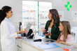 © Home-stock - Friendly female pharmacist in white coat working in the pharmaceutical store and consulting customers, mother and girl, standing at counter