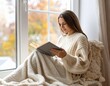 © Rookie516 - woman reading a book by the window with soft blanket