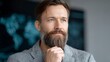 © BOJOShop - Thoughtful Caucasian man with beard and blue eyes looking away grey jacket blurred world map background