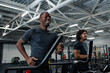© TrueFrame Collective - Low angle view of two cheerful young ethnically diverse men smiling while jogging on treadmills in modern gym