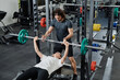 © TrueFrame Collective - Young Caucasian trainer helping sporty woman with bench press exercise in modern gym, copy space