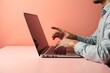 © Ariawan - Man hands texting on keyboard of laptop on pastel coral background. Minimalist style creative hipster mobile office concept. 3d rendering.
