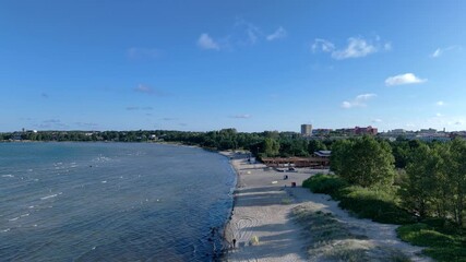 Wall Mural - Wide coastal view of sandy shoreline and calm sea under clear blue sky with city in distance