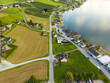 © AmazingAerialAgency - Aerial view of golden fields meet the fjord's edge, quaint houses nestled amidst lush greenery under a vast sky, a tranquil scene of rural beauty, Innvik, Vestland, Norway.