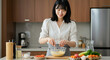 © Deezora - Young Asian Woman Whisking Ingredients in a Glass Bowl in a Modern Kitchen.