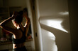 © waragron - A woman adjusts her hair in a sunlit room, creating a beautiful shadow on the wall, emphasizing her silhouette and the warm ambiance.